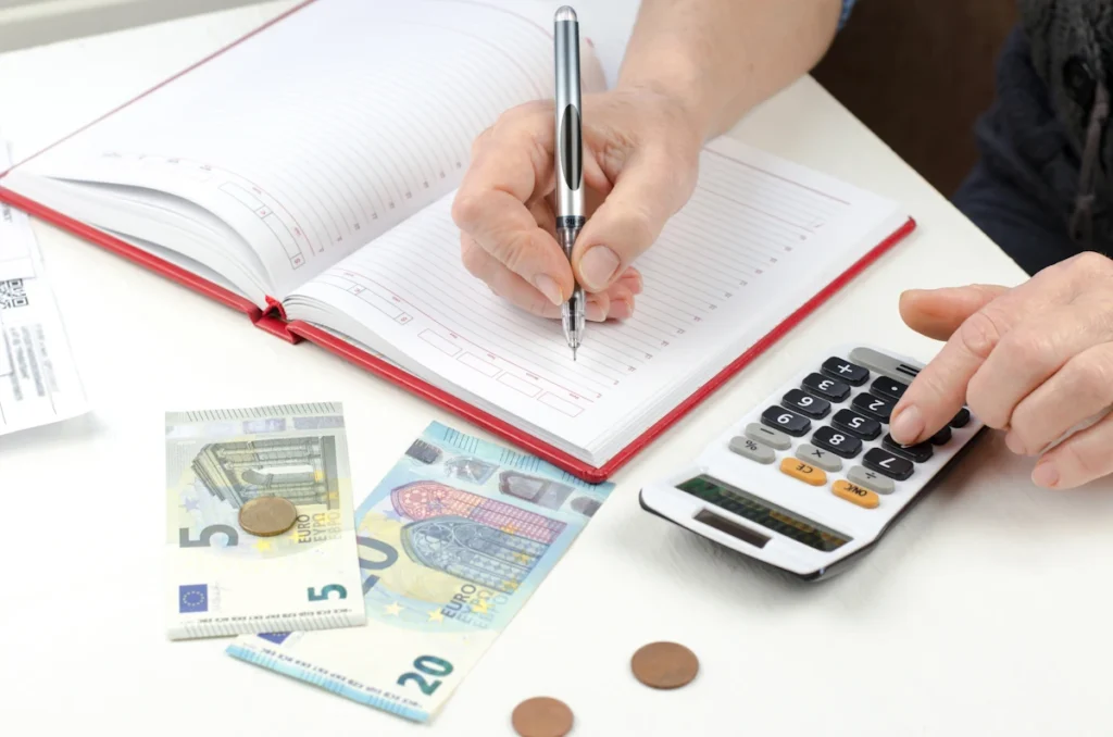 Une personne qui prend des notes et qui fait des calculs sur une calculatrice avec de l'argent sur la table