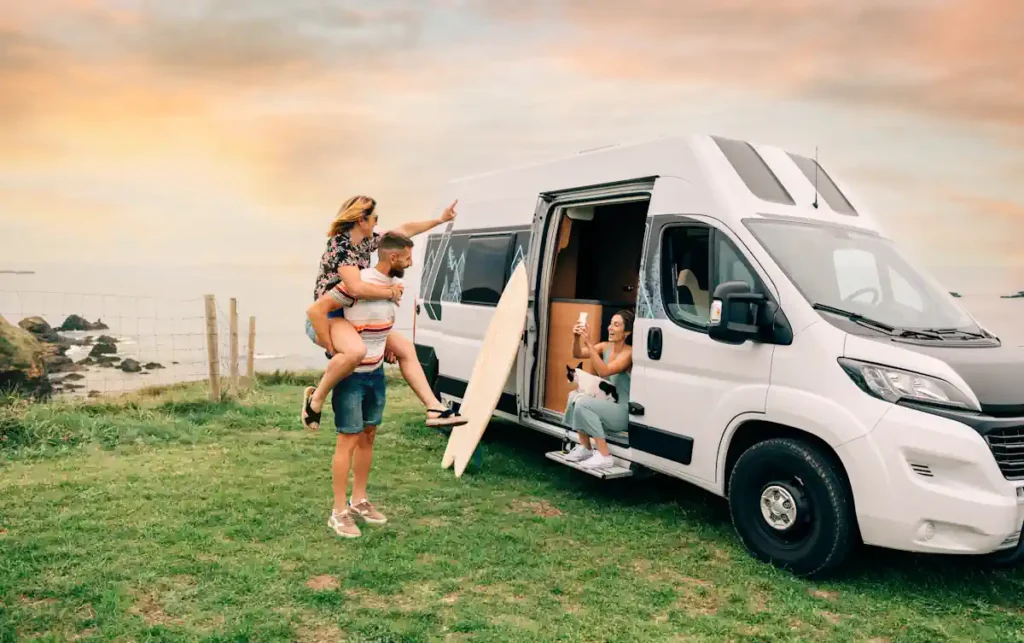 Une jeune femme sur le dos d'un jeune homme pris en photo par une autre jeune femme dans un camping-car blanc