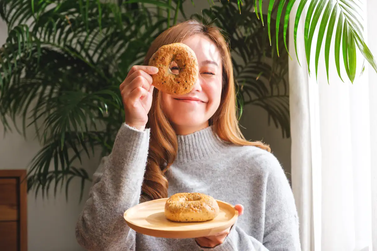 Une jeune femme qui regarde à travers un bagel en tenant une assiette avec un bagel à l'intérieur