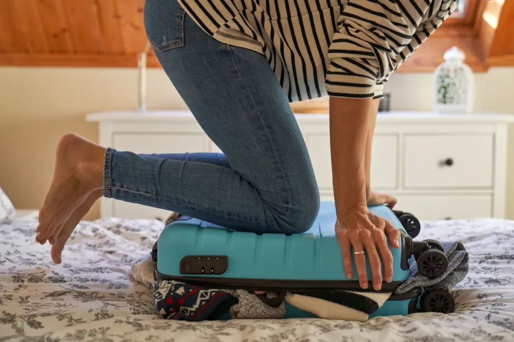 Une femme qui essaie de fermer sa valise en se tenant dessus