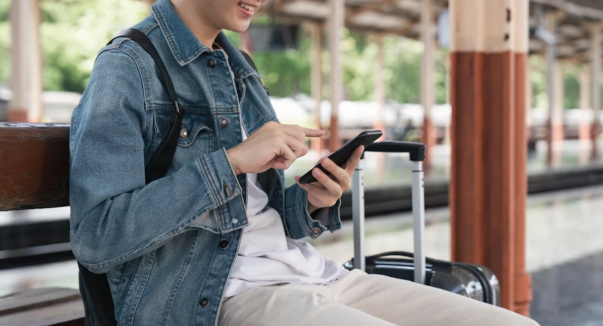 Un homme qui regarde son téléphone assis à une station avec sa valise à côté