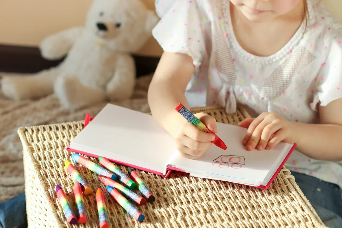 Une petite fille qui dessine avec des crayons de couleur sur un carnet