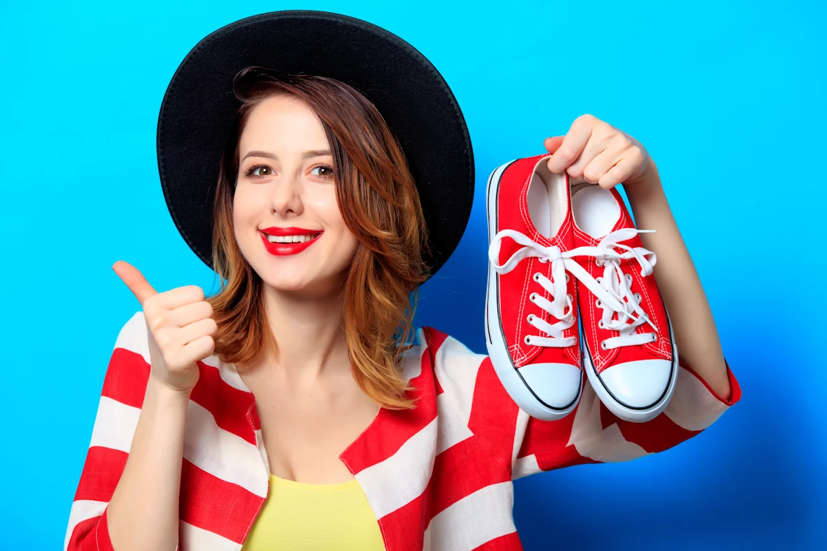 Une femme qui tient une paire de basket dans une main et lève le pousse de l'autre